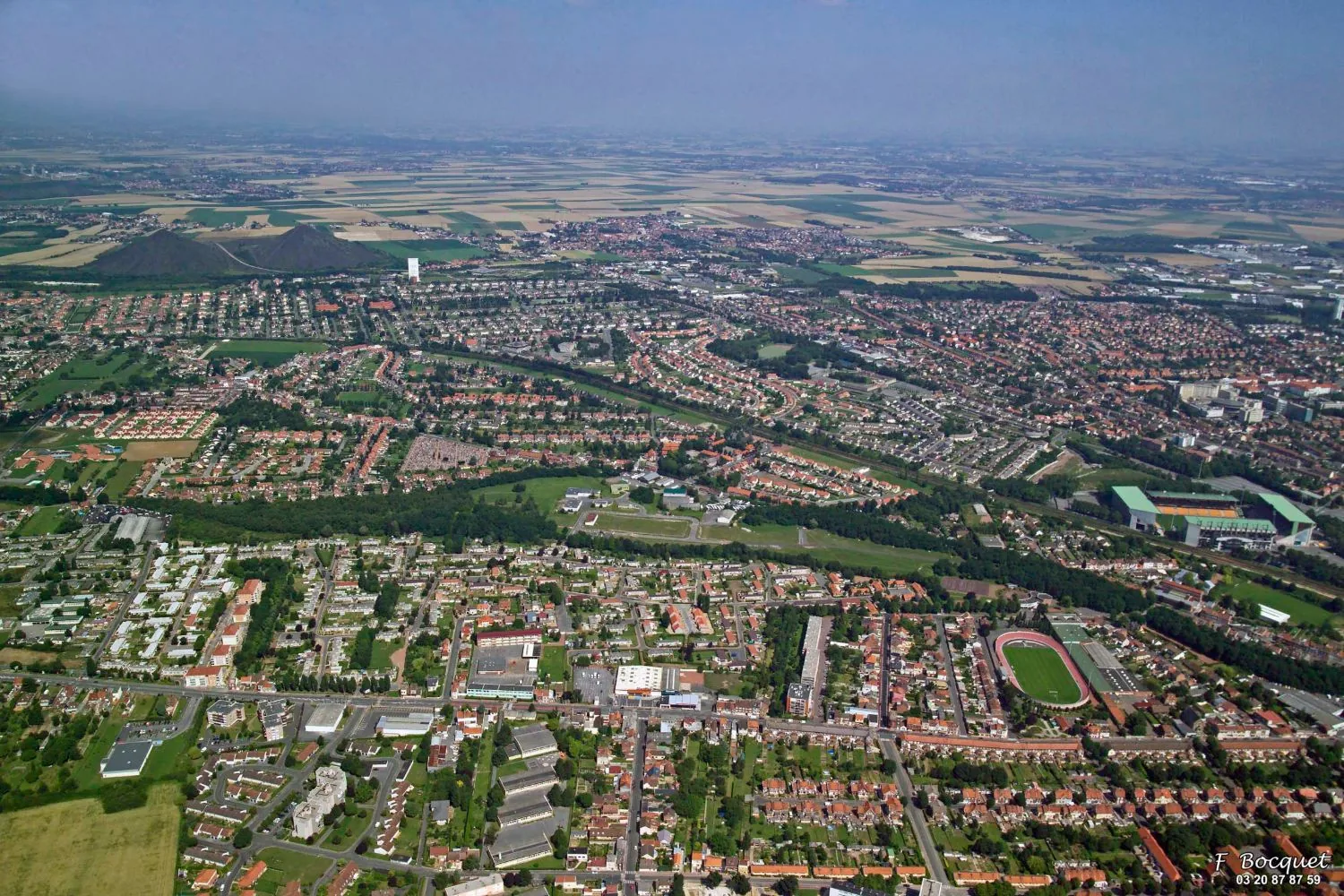 Vue aérienne de Lens en 2005 : la bande boisée de l'ancienne fosse 9, le stade Bollaert à droite, les terrils jumeaux du 11/19 au fond
