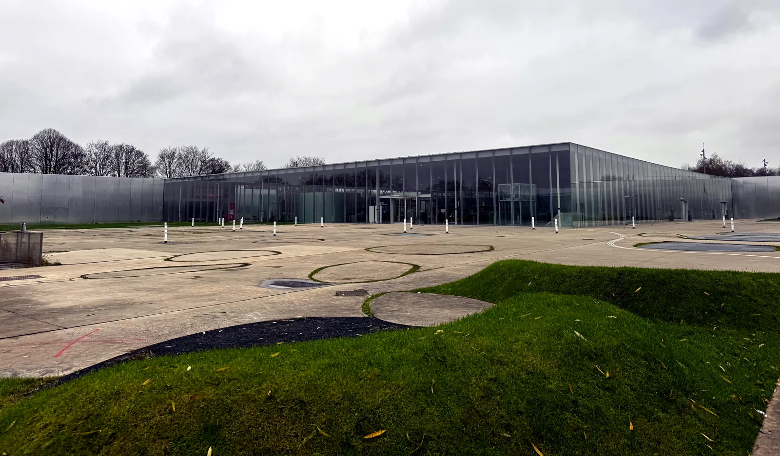 Le Louvre-Lens vu du parvis : longue façade basse de verre et d'aluminium, sol dessiné et buttes herbeuses